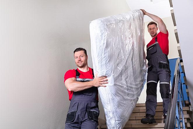 two workers carrying a heavy box spring out of a bedroom in Dale City